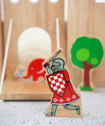 Lanka Kade red knight with raised sword figure with a wooden castle, trees and Babipur elephant figure in the background.