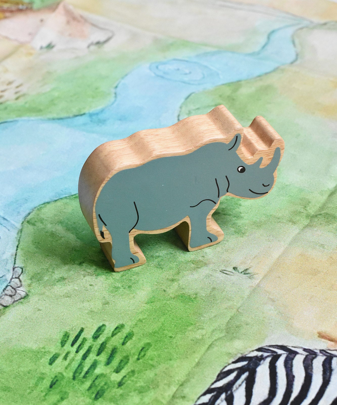 A Lanka Kade Grey Rhino Wooden Wild Animal Figure placed on a Wonderie Plains of Africa play cloth. These wooden toy figures are part of a huge range of Lanka Kade fair trade, wooden toys available here at Babipur.