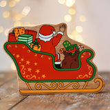 Back of the Lanka Kade Father Christmas in a sleigh wooden toy figure. The back features Santa sitting in the sleigh waving, surrounded by gifts. 