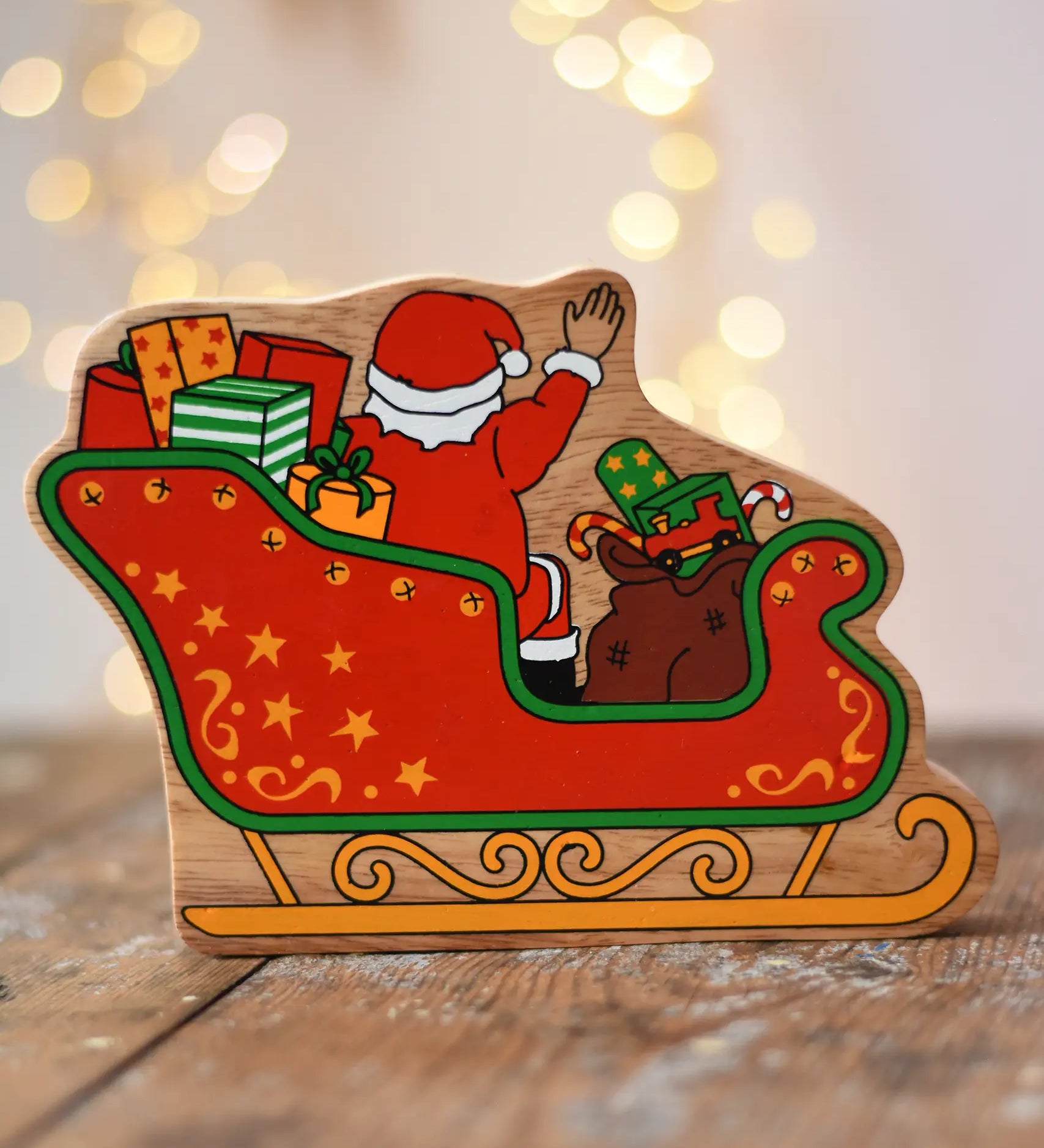 Back of the Lanka Kade Father Christmas in a sleigh wooden toy figure. The back features Santa sitting in the sleigh waving, surrounded by gifts. 