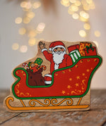 Lanka Kade Father Christmas in a sleigh wooden toy figure. The front features Santa sitting in the sleigh waving, surrounded by gifts. 