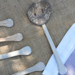 A close up of on of the utensils from the Lanka Kade coconut shell utensil set. The mesh storage bag that the set comes in can be seen to one side along with the handles from other utensils.