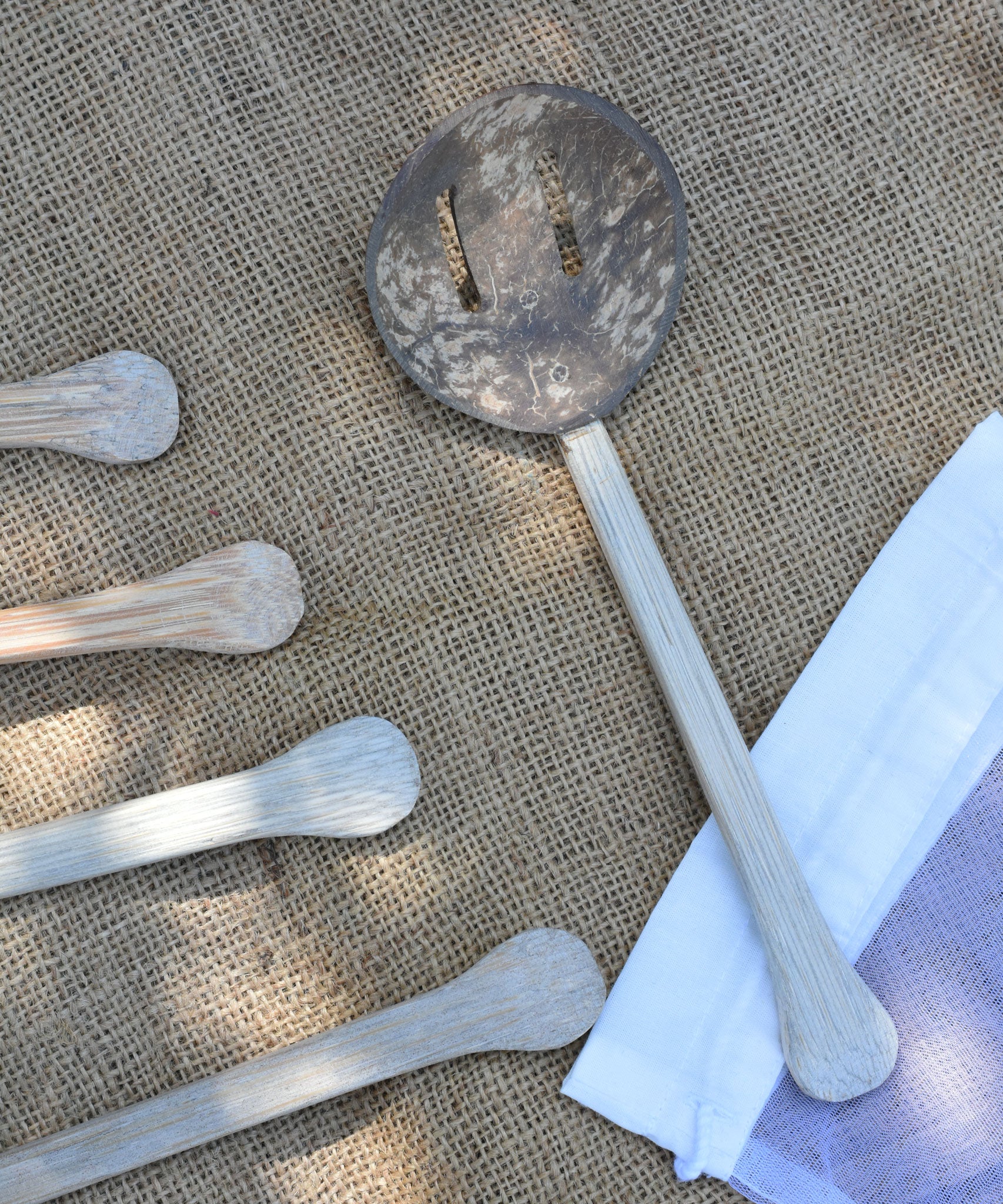 A close up of on of the utensils from the Lanka Kade coconut shell utensil set. The mesh storage bag that the set comes in can be seen to one side along with the handles from other utensils.