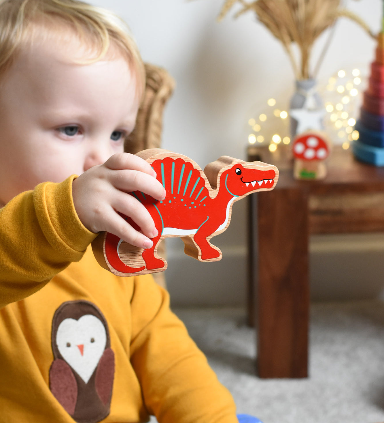 A child holding the Lanka Kade Wooden Spinosaurus Dinosaur in their hand. These wooden toy figures are part of a huge range of Lanka Kade fair trade, wooden toys available here at Babipur.
