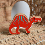 A red Lanka Kade Wooden Spinosaurus Dinosaur placed on a child's wicker chair. These wooden toy figures are part of a huge range of Lanka Kade fair trade, wooden toys available here at Babipur.

