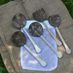 The 5 utensils from the Lanka Kade Coconut Shell Utensil Playset laid out on top of the mesh storage bag that they are supplied in. 
