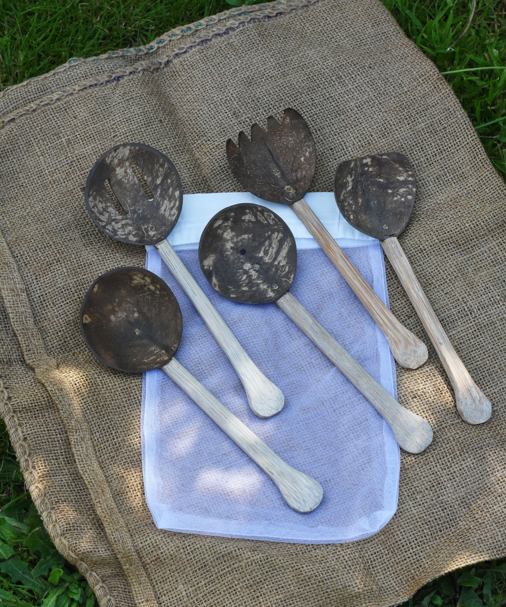 The 5 utensils from the Lanka Kade Coconut Shell Utensil Playset laid out on top of the mesh storage bag that they are supplied in. 