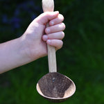 The ladle spoon utensil from the Lanka Kade coconut shell utensil set shown in a child's hand. 