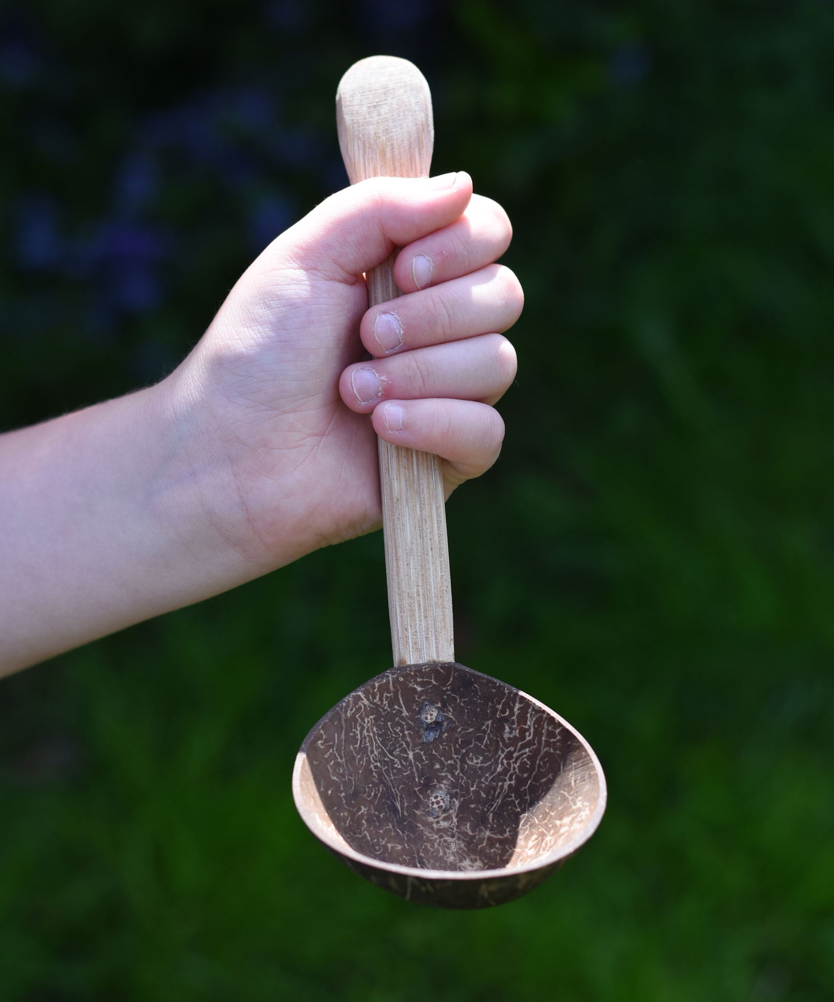 The ladle spoon utensil from the Lanka Kade coconut shell utensil set shown in a child's hand. 