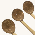 A close up of the coconut spoons from the coconut water play set showing the 3 small shells on a wooden handle with holes in the bottom for water to pour through them