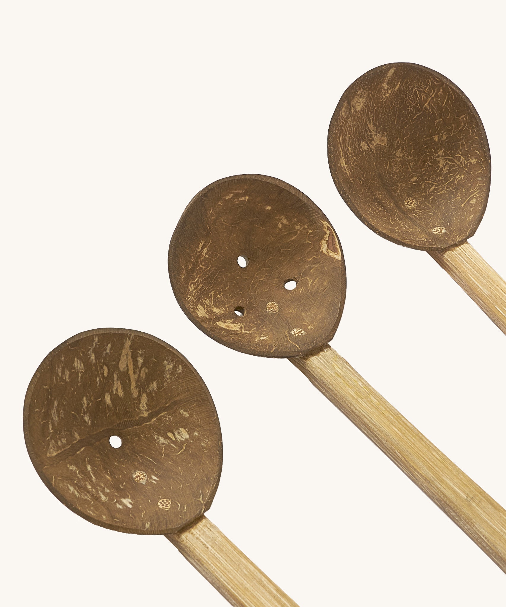 A close up of the coconut spoons from the coconut water play set showing the 3 small shells on a wooden handle with holes in the bottom for water to pour through them
