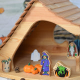 A Lanka Kade witch and cauldron wooden toys placed in the Ostheimer wooden cottage with other wooden toys such as Bumbu pumpkins around them.