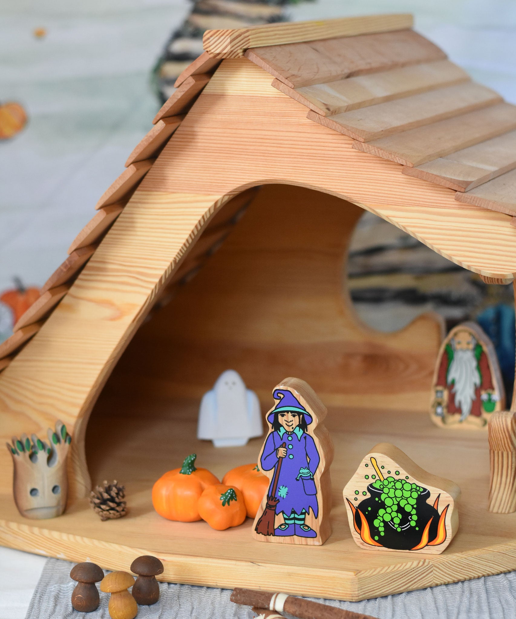 A Lanka Kade witch and cauldron wooden toys placed in the Ostheimer wooden cottage with other wooden toys such as Bumbu pumpkins around them.