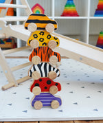 Lanka Kade wooden animal printed cars stacked on a playmat next to a Triclimb wooden slide and wooden climbing frame. Features a bumblebee, leopard, tiger, zebra, ladybird and beetle printed wooden car.