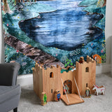 A Lanka Kade wooden toy castle placed on a carpeted floor in front of a Wonderie Moonlight Forest design play cloth that's been hung on the wall behind. Fairytale themed wooden toy character figures have been placed in and around the wooden toy castle. 