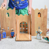 The Lanka Kade wooden toy fairytale castle play set shown with the wooden character figures in and around the castle. A witch, wizard, prince, fairy, unicorn and dragon can be seen standing in front of the castle, whilst a princess can be seen peering through one of the windows of the castle. 