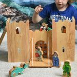 A child playing with the Lanka Kade Fairytale castle playset. The fairytale themed wooden character figures have been placed in and around the toy castle. 