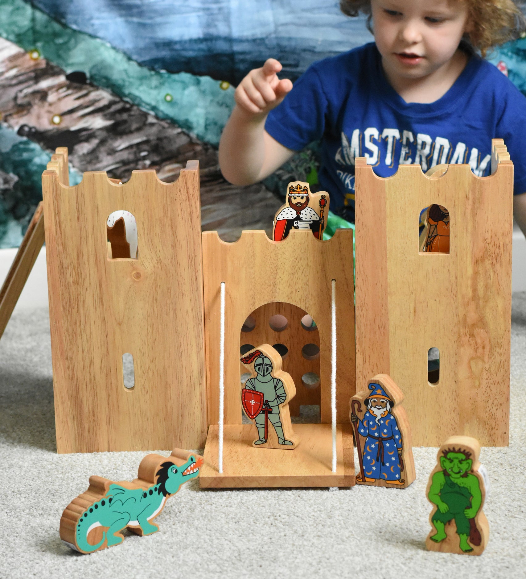 A child playing with the Lanka Kade Fairytale castle playset. The fairytale themed wooden character figures have been placed in and around the toy castle. 