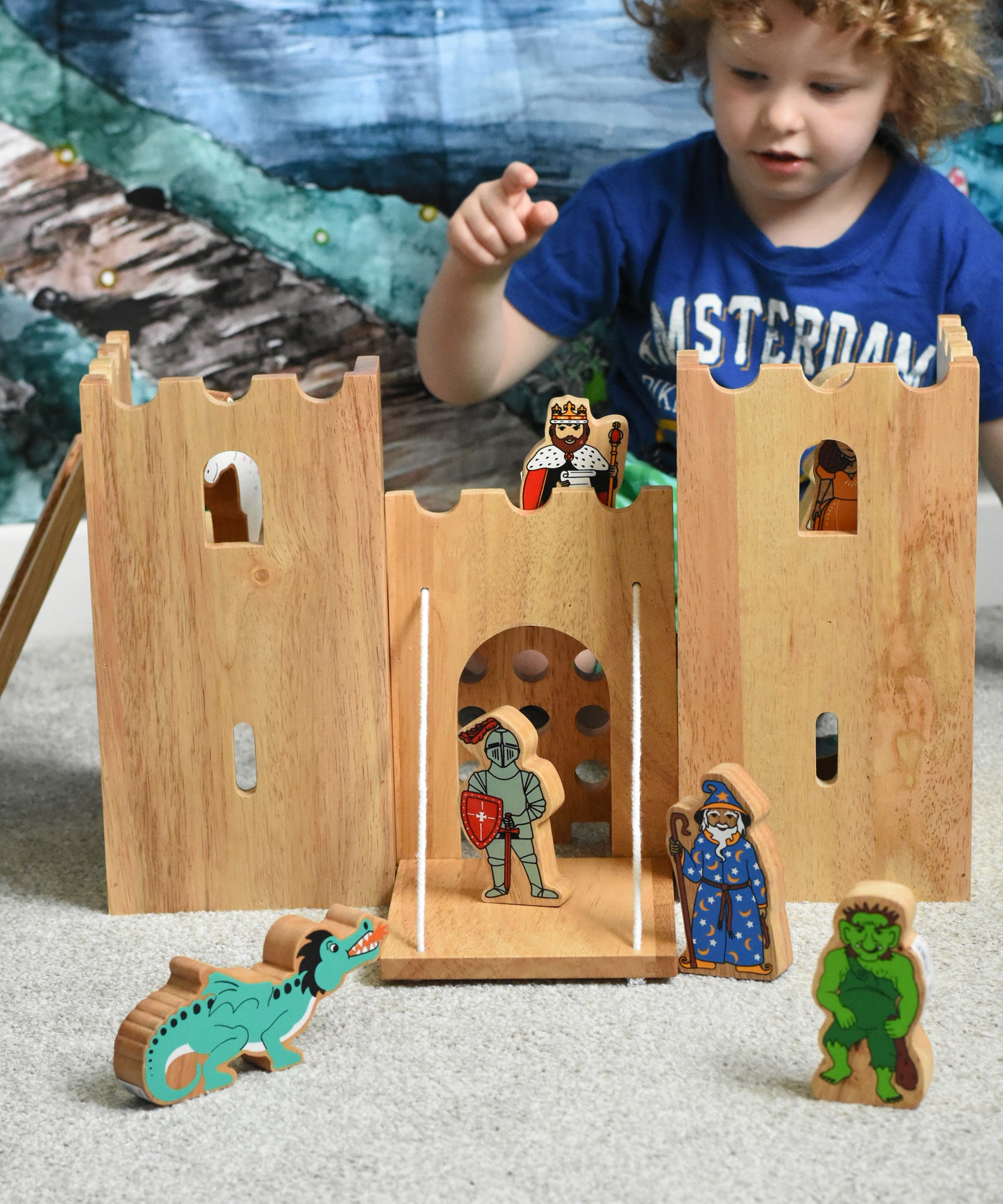 A child playing with the Lanka Kade Fairytale castle playset. The fairytale themed wooden character figures have been placed in and around the toy castle. 