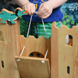 A close up of  child pulling the string to close the drawbridge on the Lanka Kade wooden castle. A green dragon figure can be seen on the castle walls.