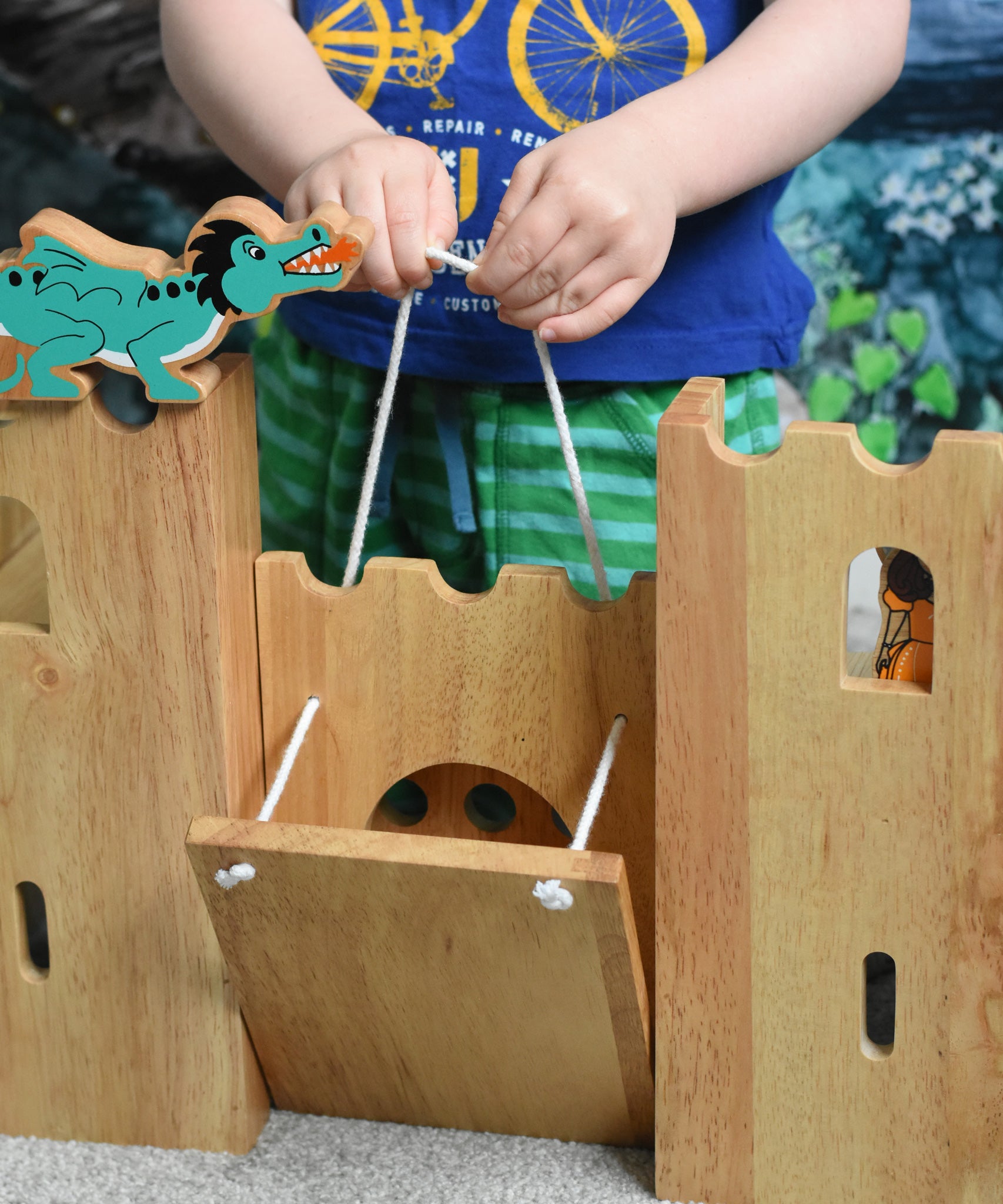 A close up of  child pulling the string to close the drawbridge on the Lanka Kade wooden castle. A green dragon figure can be seen on the castle walls.
