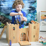 A child playing with the Lanka Kade wooden toy fairytale castle play set. A Wonderie moonlight forest can be seen hung on the wall in the background. 