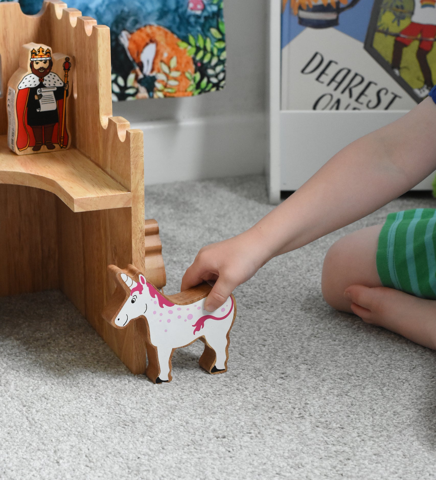 A close up of a Lanka Kade wooden unicorn figure in a child's hand. The Lanka Kade wooden toy castle can be seen in the background.