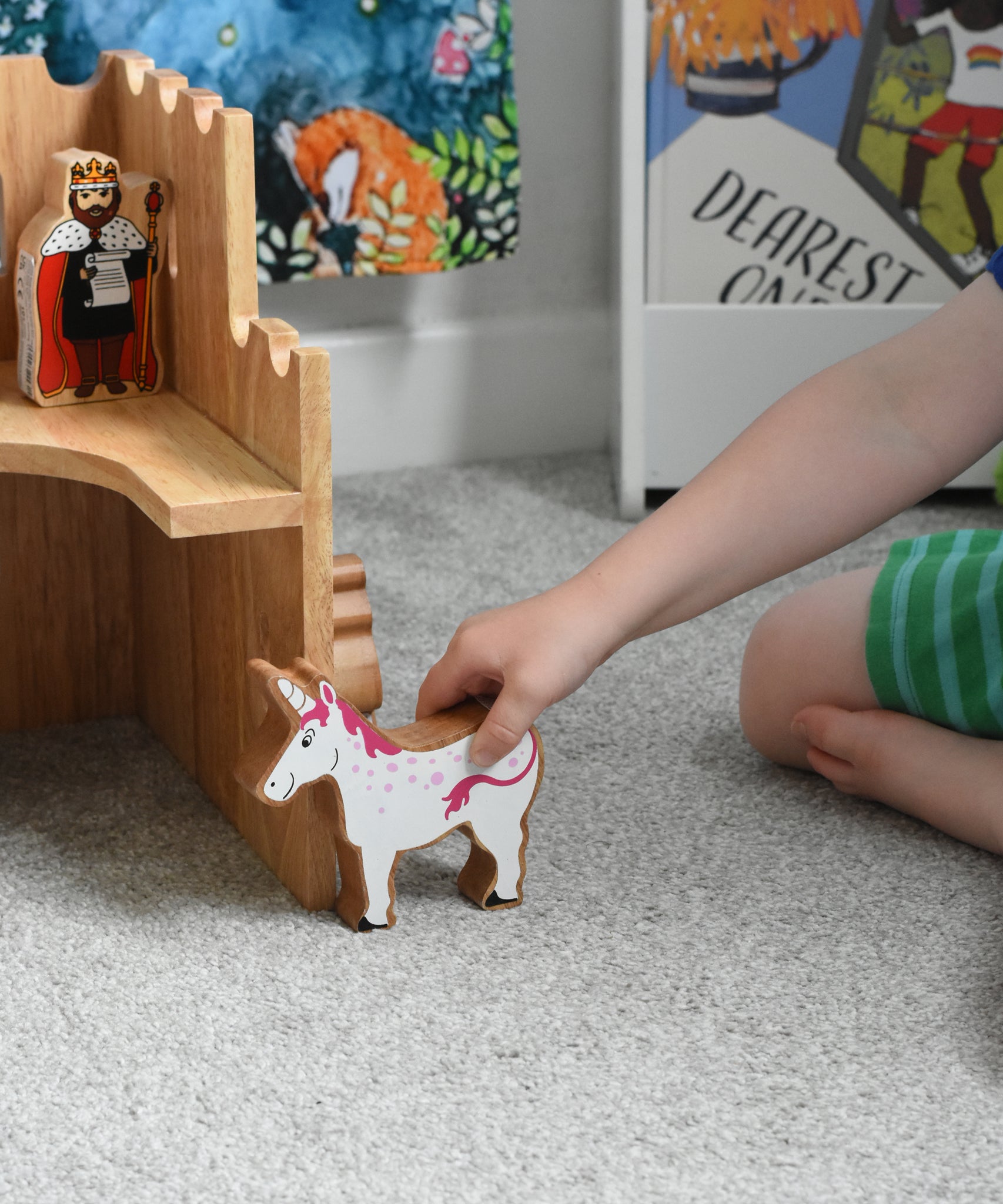 A close up of a Lanka Kade wooden unicorn figure in a child's hand. The Lanka Kade wooden toy castle can be seen in the background.