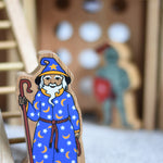 A Lanka Kade wooden toy wizard figure. The wizard has a blue coloured cloak with white and yellow stars and moon pattern withe a matching hat. The wizard is also holding a tall brown stick. 