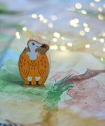 A Lanka Kade Wooden Yellow and White Vulture Toy placed on a Wonderie play cloth with fairy lights in the background. These wooden toy figures are part of a huge range of Lanka Kade fair trade, wooden toys available here at Babipur.