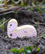 Lanka Kade Wooden Worm Toy is having an adventure outside in the soil!  The worm had a pink with brown lines on its body and a smiling face