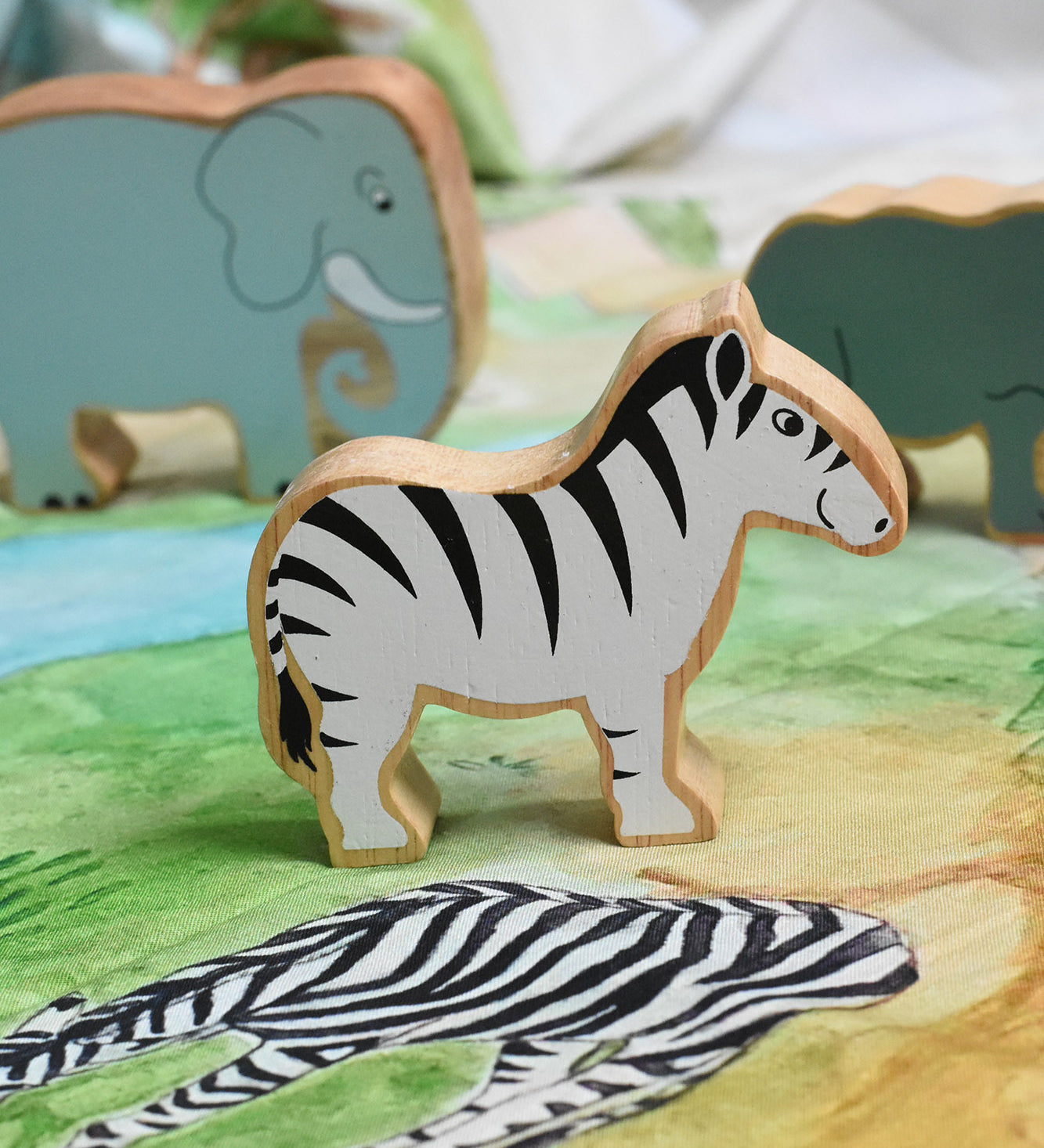 A Lanka Kade Zebra wooden toy figure placed on a Wonderie plains of Africa play cloth. These wooden toy figures are part of a huge range of Lanka Kade fair trade, wooden toys available here at Babipur.