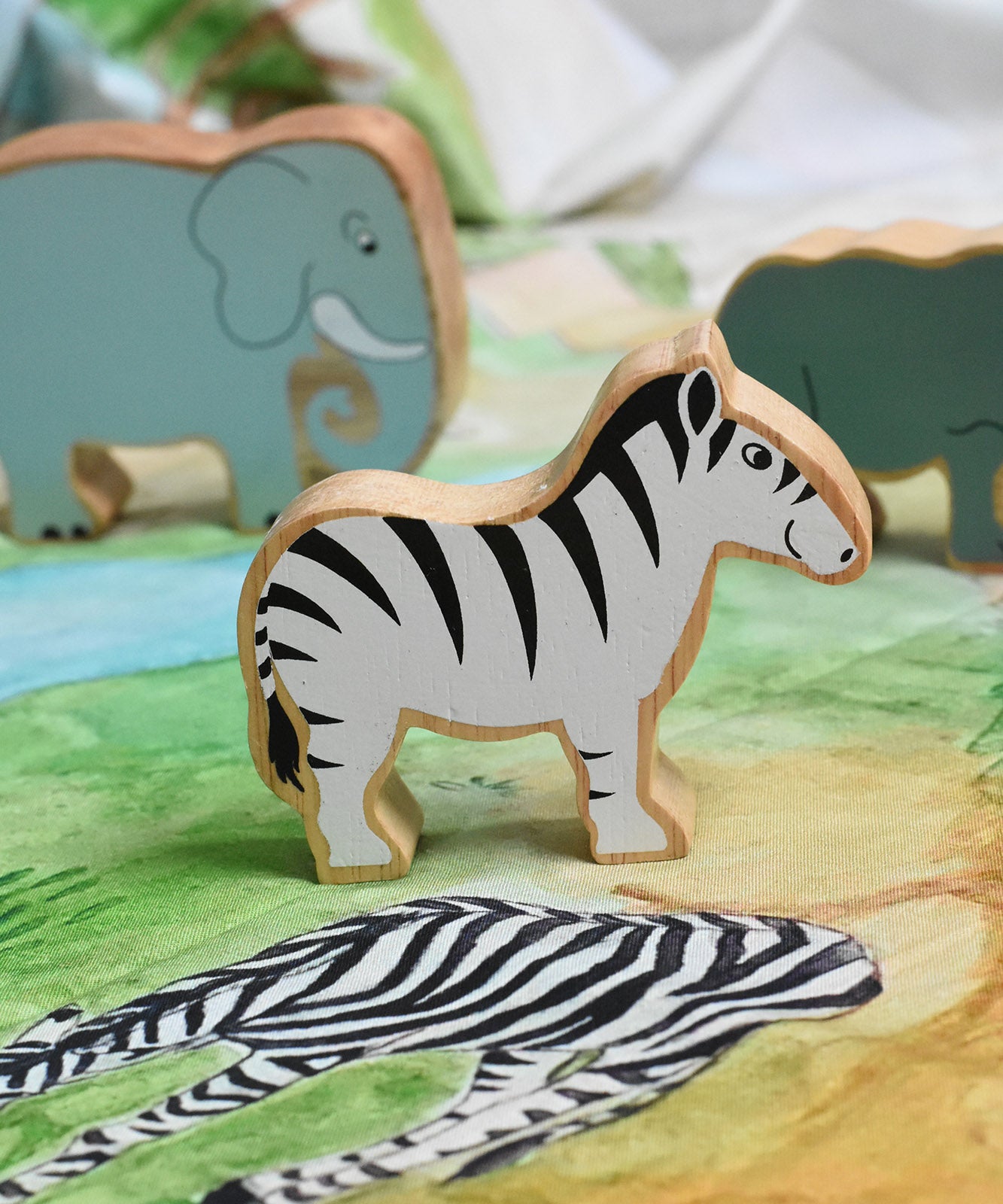 A Lanka Kade Zebra wooden toy figure placed on a Wonderie plains of Africa play cloth. These wooden toy figures are part of a huge range of Lanka Kade fair trade, wooden toys available here at Babipur.