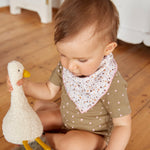 A little baby playing with a goose toy, and wearing the Lassig organic cotton bandana bib. 