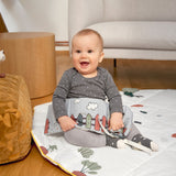 A smiling baby holding the Lassig Baby Touch & Feel soft toy book.
