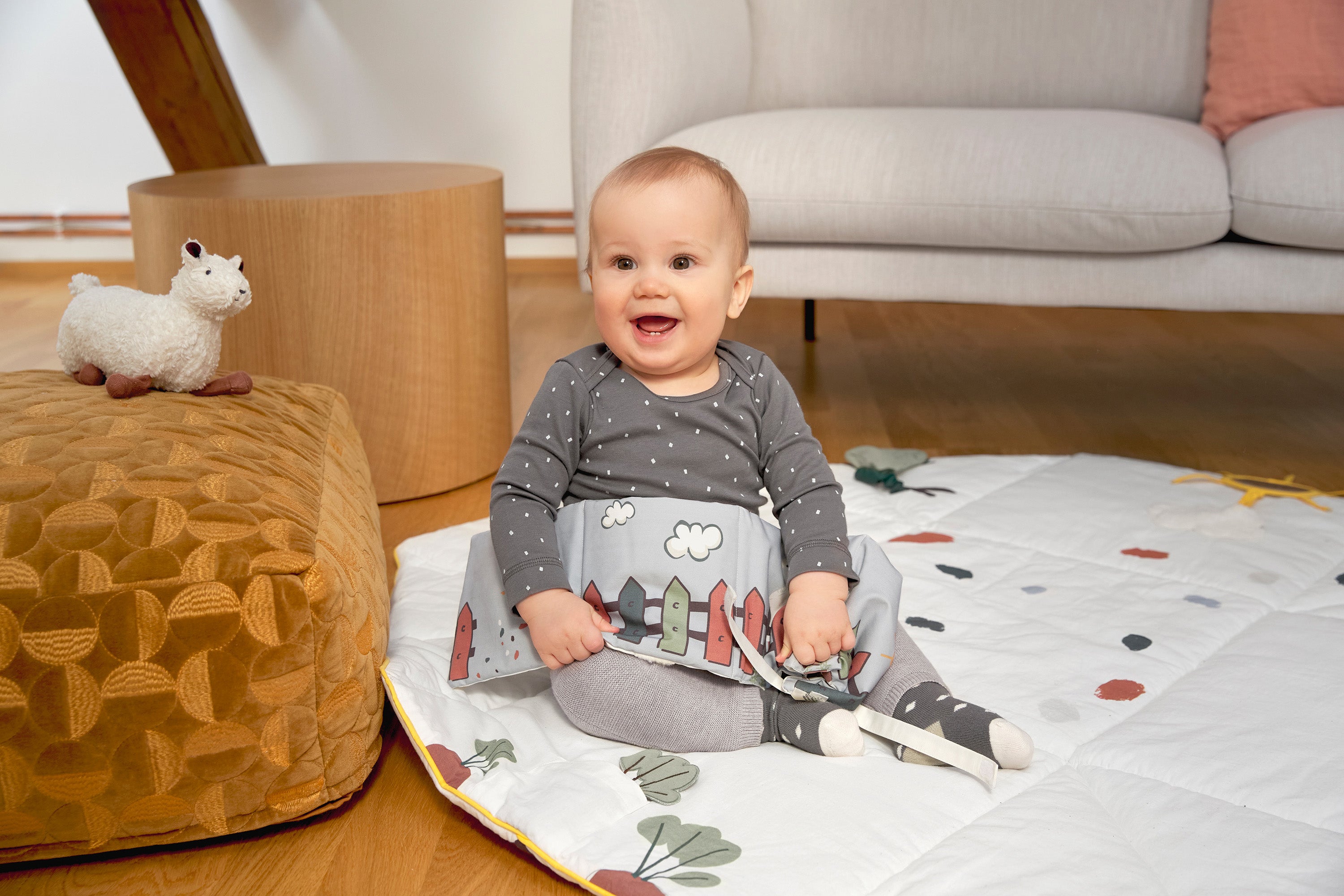 A smiling baby holding the Lassig Baby Touch & Feel soft toy book.