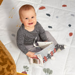 A baby smiling and holding the Lassig Baby Touch & Feel soft toy book.