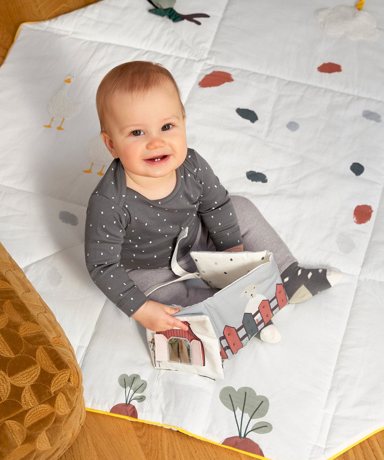 A baby smiling and holding the Lassig Baby Touch & Feel soft toy book.