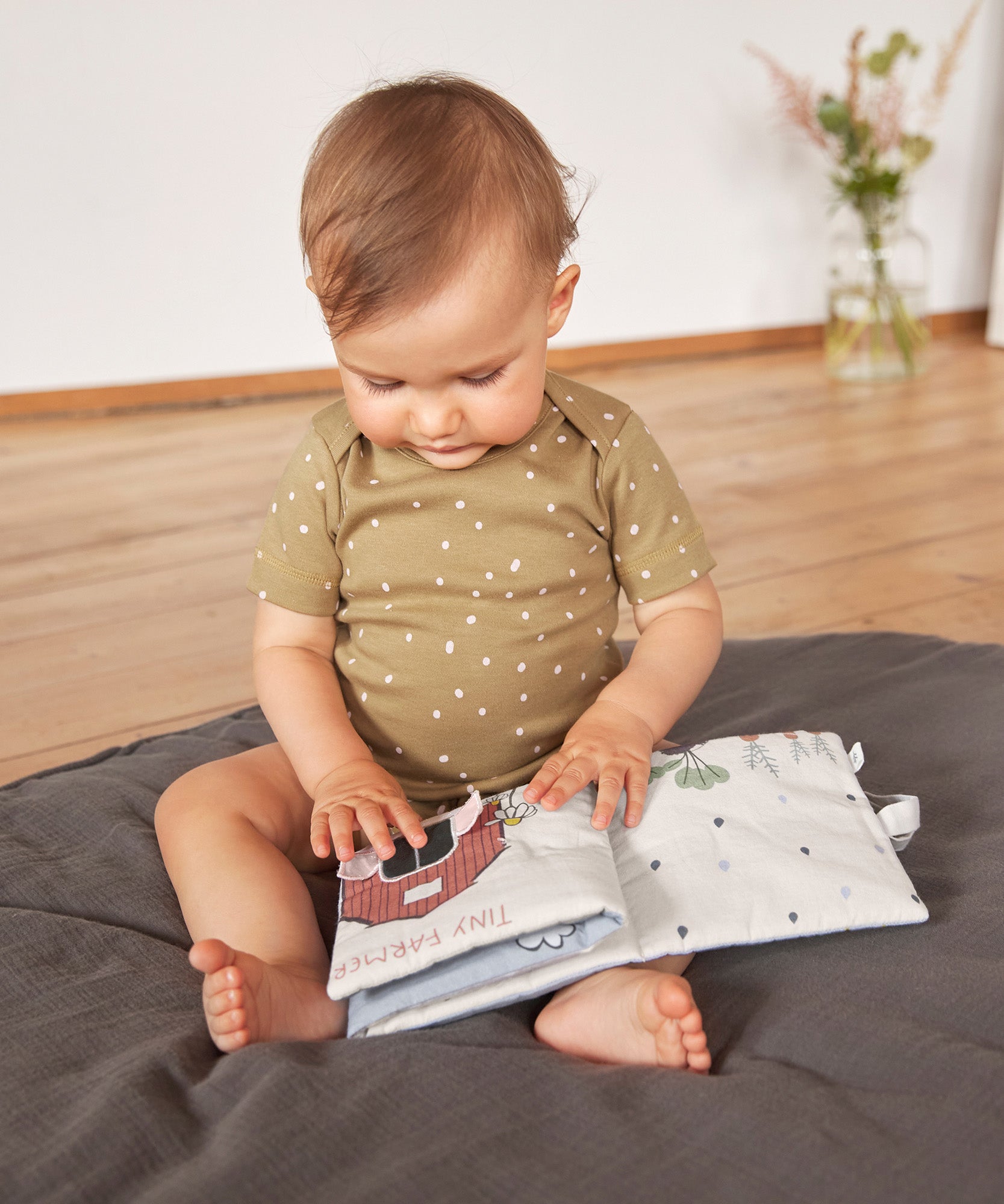 A little baby touching the Lassig Baby Touch & Feel soft toy book.