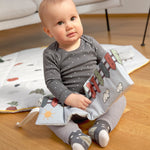 A little baby sitting down and holding the Lassig Baby Touch & Feel soft toy book.