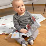 A little baby sitting down and holding the Lassig Baby Touch & Feel soft toy book.