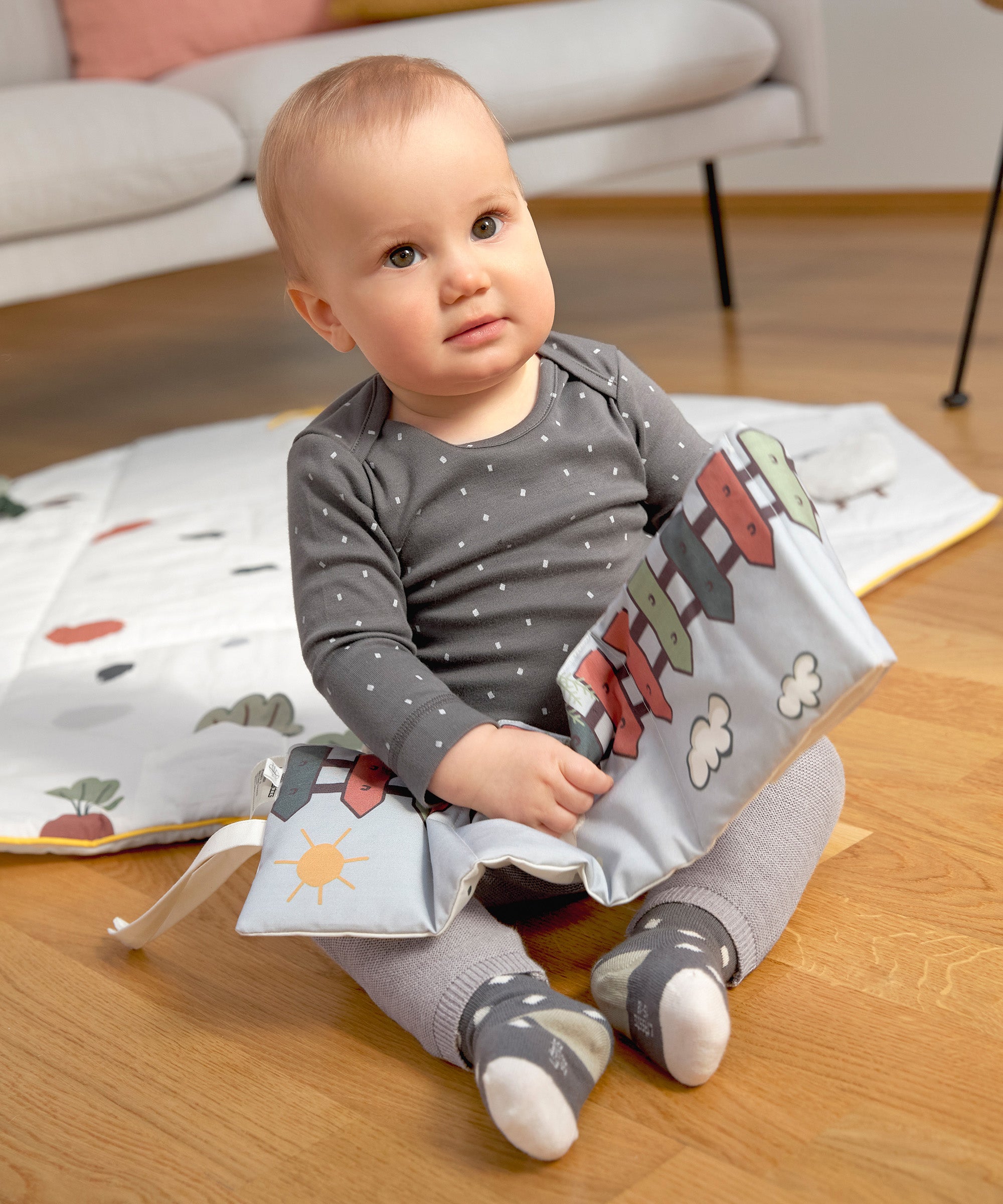 A little baby sitting down and holding the Lassig Baby Touch & Feel soft toy book.