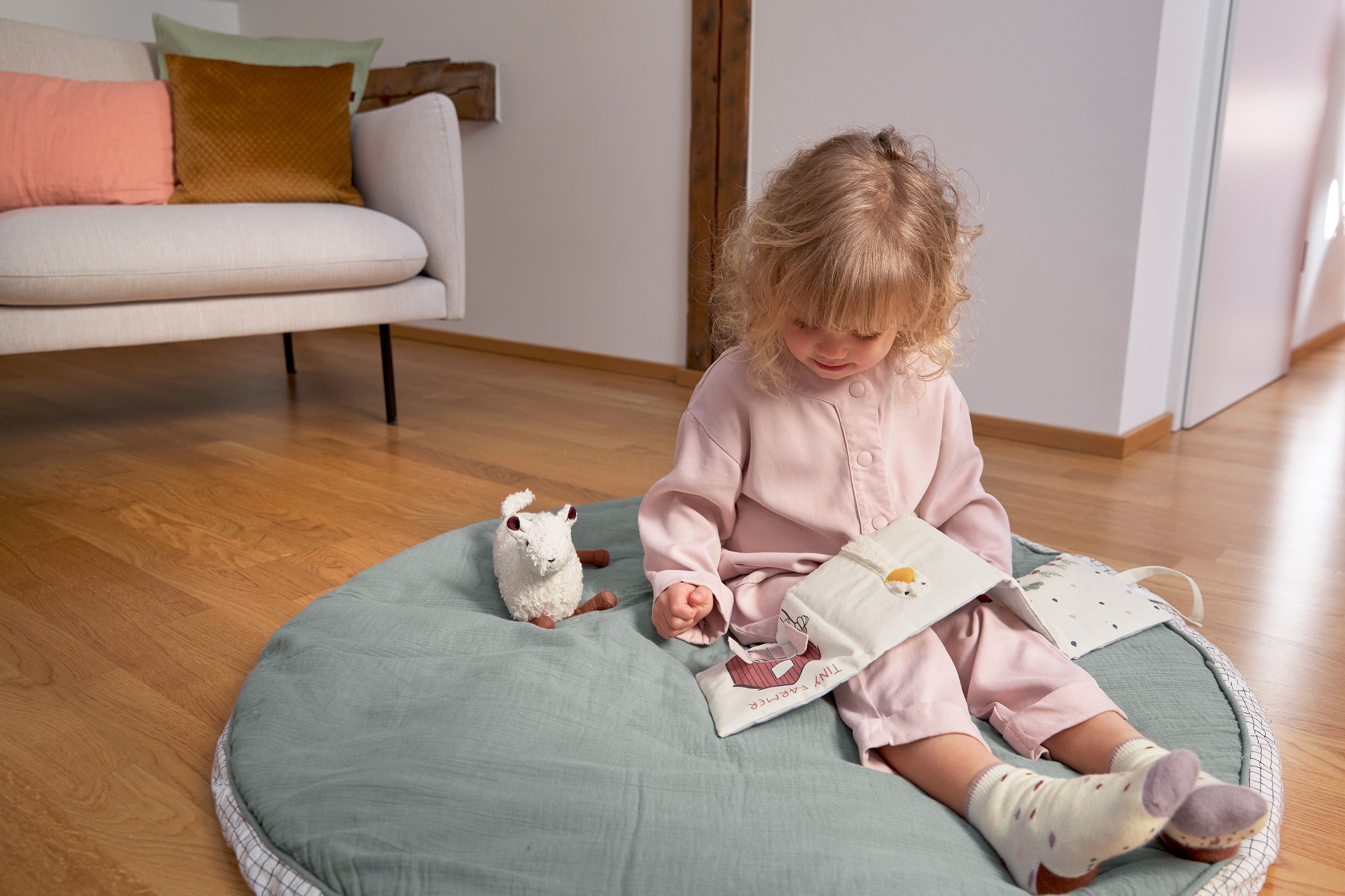A little girl reading the Lassig Baby Touch & Feel soft toy book.