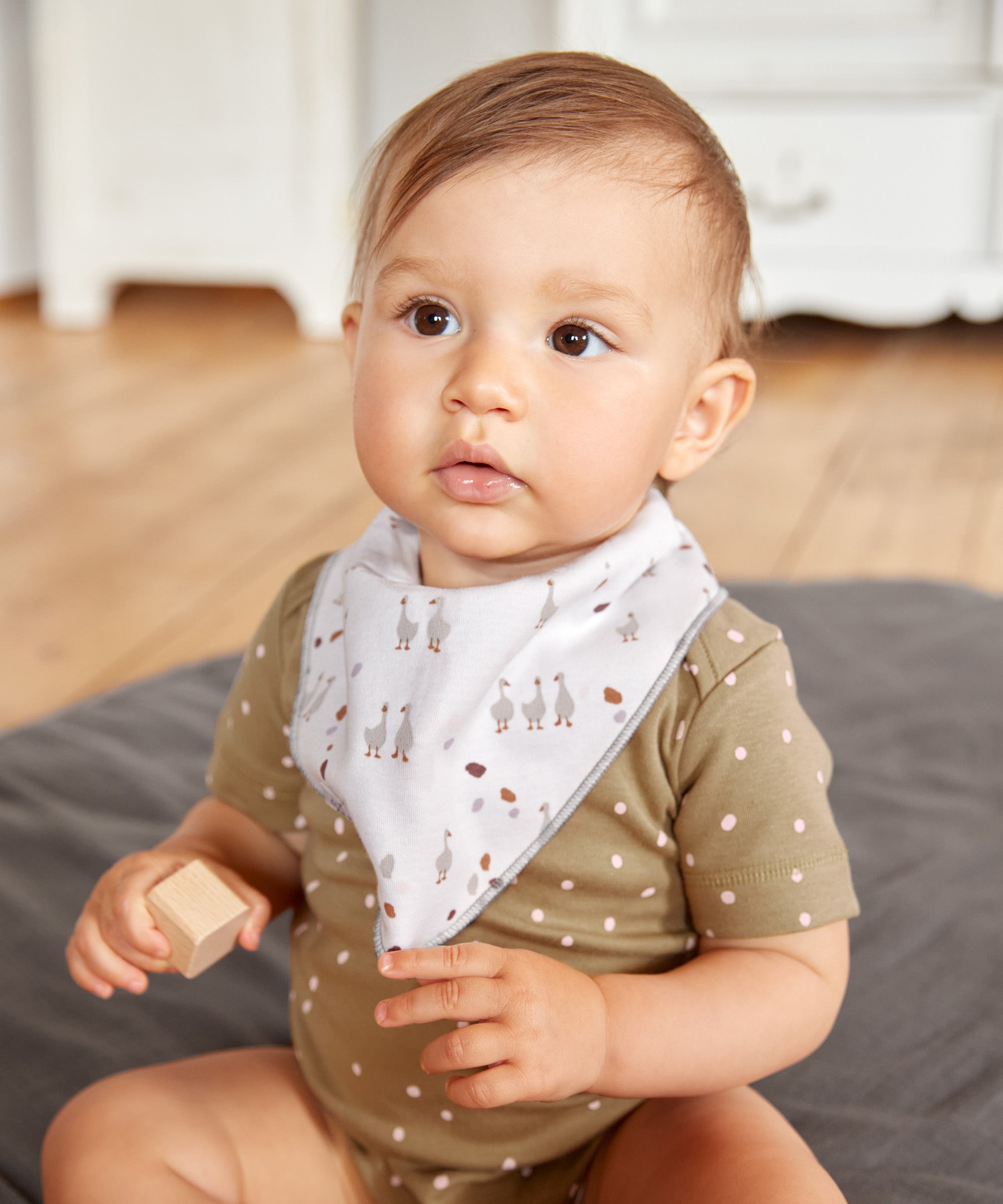 A baby wearing the Lassig organic bandana dribble bib, in white with little geese printed all over. 