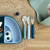 The Lassig Cutlery with Silicone Handle with a Tiny Team Dog design shown on a table ready to be used. These green and blue coloured children's cutlery are part of a wide range of tabelware avaialable at Babipur.