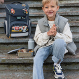 A child sitting on steps next to a filled Lassig Stainless Steel Lunchbox with a Unique Dark Blue lid. This lunch box has a removable divider. 