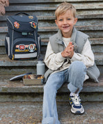 A child sitting on steps next to a filled Lassig Stainless Steel Lunchbox with a Unique Dark Blue lid. This lunch box has a removable divider. 