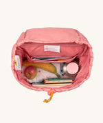 A top down viw of the interior of the Lassig Kids Big Outdoor Backpack with an Adventure rose pink design with items of clothing, fruit, books and a bottle inside. The print features tents, trees, and clouds, and a pink front strap. These children's backpacks are part of a wide range available at Babipur.