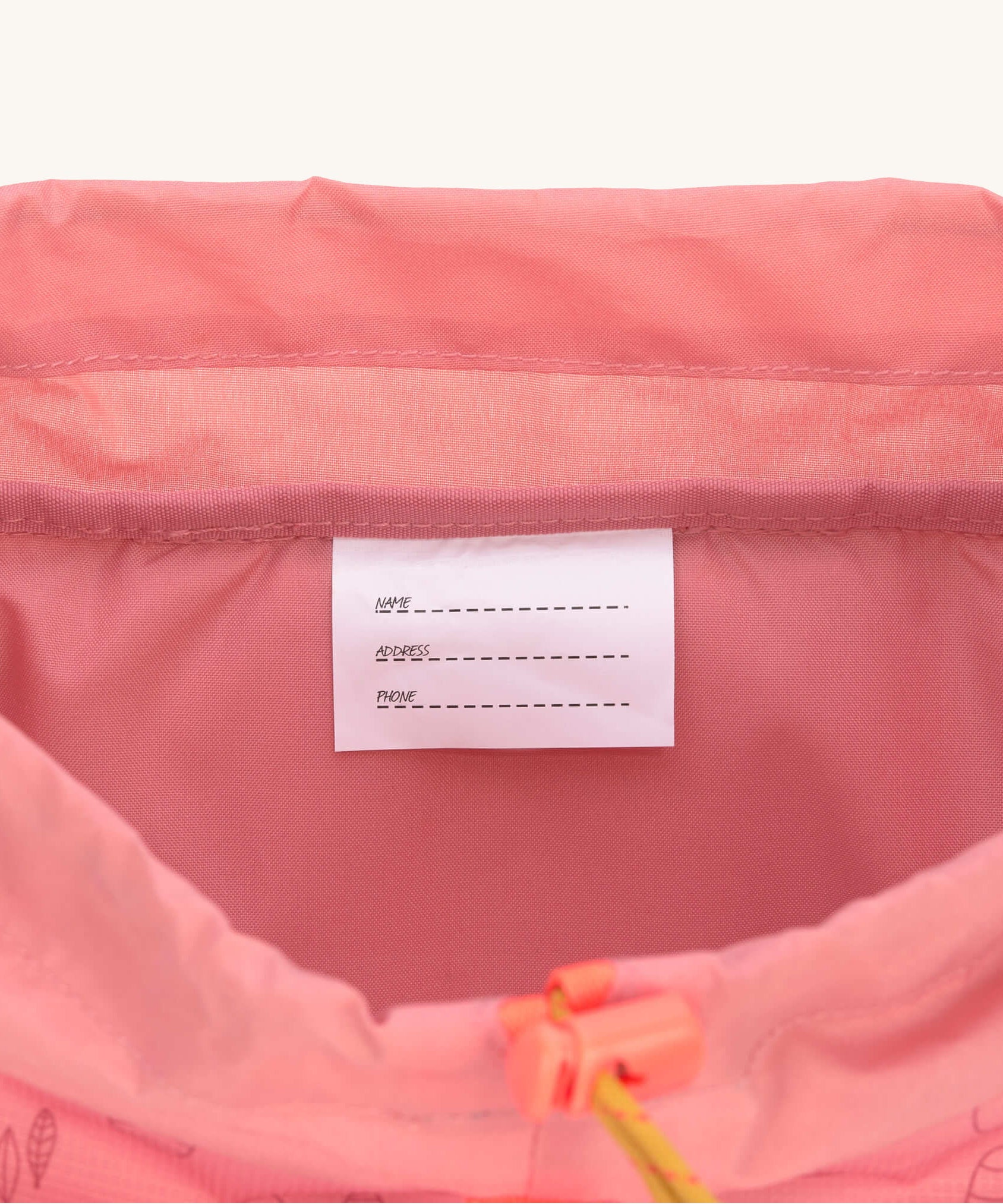 A close up of the name and details tag inside the Lassig Kids Big Outdoor Backpack with an Adventure rose pink design. The print features tents, trees, and clouds, and a pink front strap. These children's backpacks are part of a wide range available at Babipur.