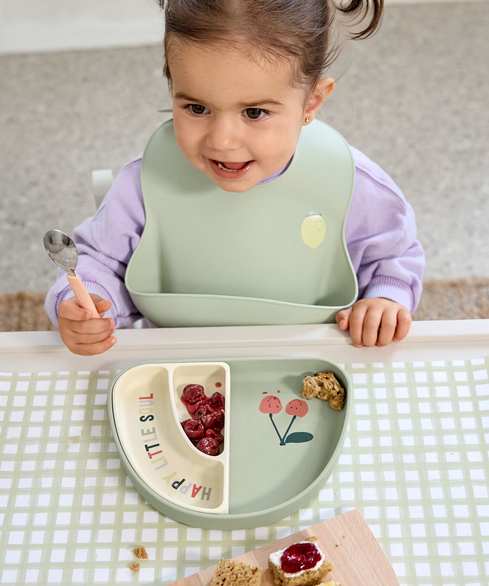 A child using the Lassig Cutlery with Silicone Handle  featuring Happy Fruits Lemon design. This children's cutlery set is part of a wide range of tableware available at Babipur.